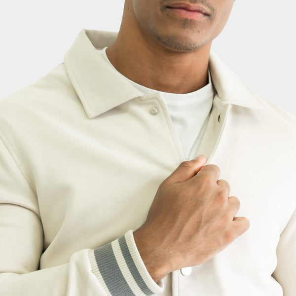 Detalle del cuello, abertura frontal y puño de la Chamarra Varsity de Gamuza color hueso | hover: Hueso
